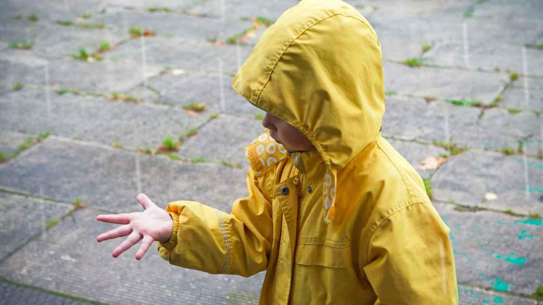 child in raincoat looking at rain